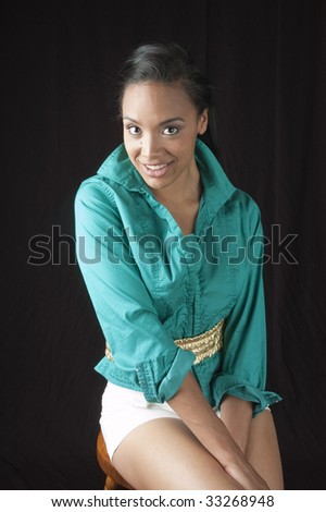 Beautiful smiling african american woman sitting on stool, isolated on black