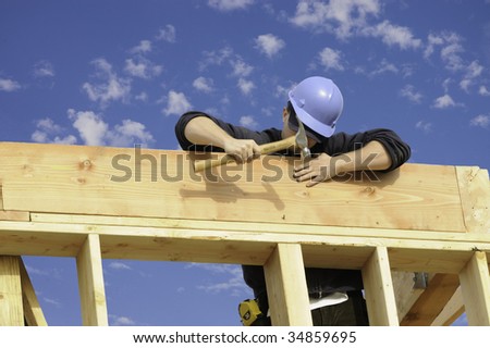Construction worker pounding in a nail against a blue sky with puffy clouds
