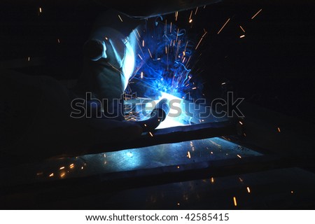 Blacksmith working on decorative handrail using welding equipment making beautiful blue light from torch