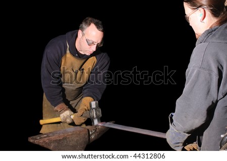 Blacksmith working on decorative handrail beating the heated metal with a sledge hammer