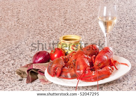 Freshly boiled lobster on a white plate with crackers, tomato, an onion a glass of wine and a napkin on a granite counter