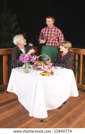 older couple in outdoor restaurant at night - waiter has served the wine to the man, to see if it is acceptable, from the look on his face it meets his requirements and is satisfactory:)