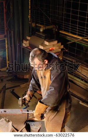 Blacksmith working on decorative handrail after heating it up to  a cherry red, he is beating on it to form it into shape