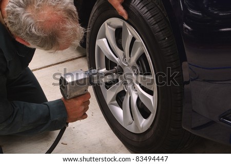 Mechanic working on car using an air impact tool to change tires on a vehicle.