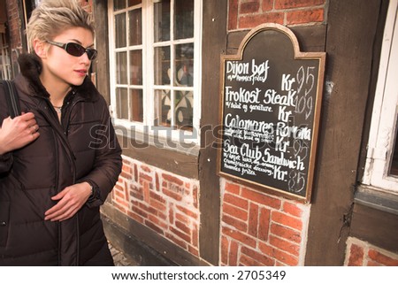 pretty woman outdoor in an old village in denmark looking at a restaurant menu card outside the building