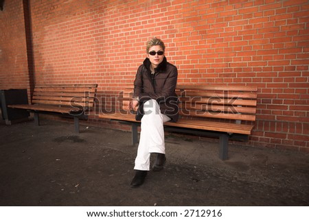 pretty woman outdoor, sitting on a bench  in an old village in denmark with a wall   in red brick