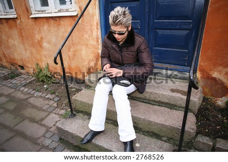 pretty woman outdoor in an old village in denmark sitting on the staircase of an old house mobile phone in hands and looking into her bag