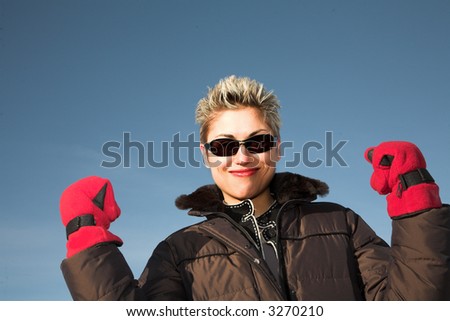 woman outdoor in winter shot against a blue sky in the sun playing with red gloves