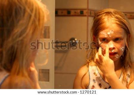 Little girl creaming her face in front of  a mirror in golden-orange light