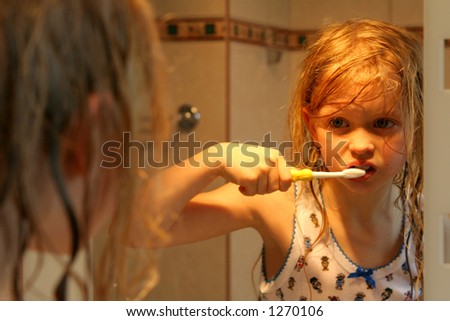 Little girl brushing teeth in front of  a mirror in golden-orange light
