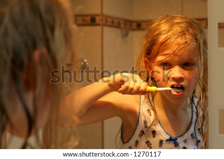 Little girl brushing teeth in front of  a mirror in golden-orange light