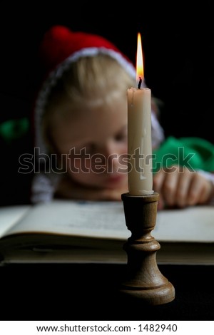 Little girl reading a book. Focus on candle