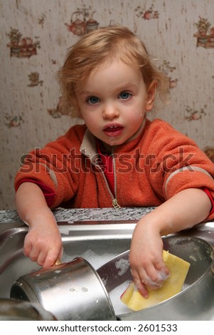 Little baby washing the dishes in the kitchen