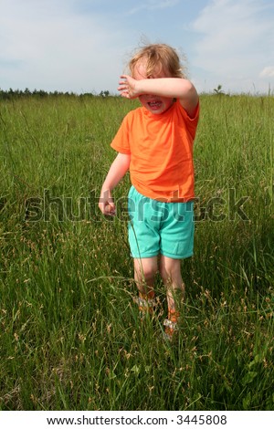 Little crying girl in an orange t-shirt in the meadow