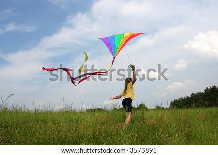 Children flying rainbow kite in the meadow on a blue sky background