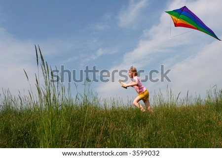 Children flying rainbow kite in the meadow on a blue sky background