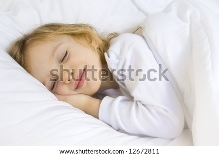 Little blond girl wearing white blouse in white bedclothes