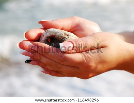 female hands with sea pebbles on the sea background