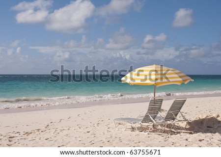 Two Lounge Chairs, and umbrella, beautiful pink sand beach, and crystal clear water on a beautiful sunny day.