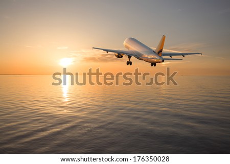 The airplane climbs, flying over the sea towards the sun at sunset
