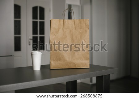 Photo blank: disposable bag of kraft paper on a wooden table and cup of coffee
