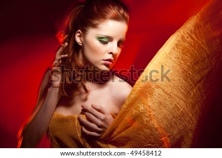 Beautiful red-hair young woman covered in orange cloth in red lights