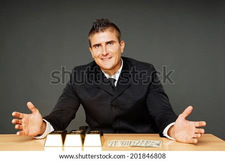 Young businessman in suit shows with his hands on money and gold brick