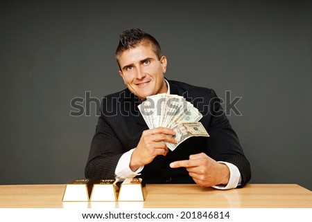 Young businessman in suit shows you money and gold brick