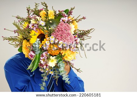 Young businessman holds front of his face bouquet of flowers with autumn decoration