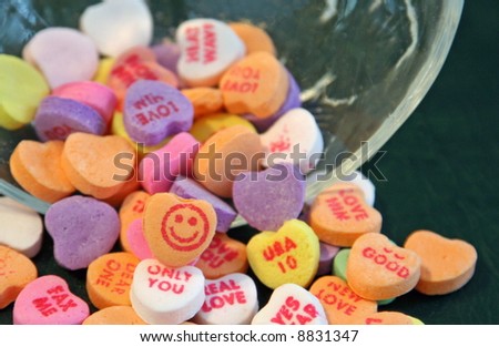 Valentine candy hearts spilling from a glass dish with focus on happy face.