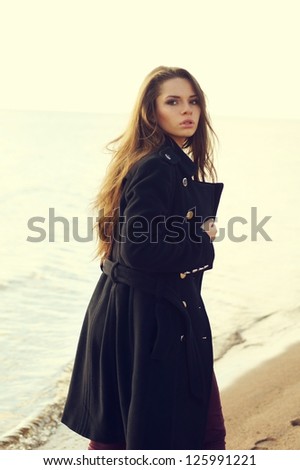 fashion portrait. woman in coat walking at coast and looking in camera backside