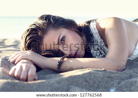fashion face portrait of young beautiful woman lying at the sand of the beach