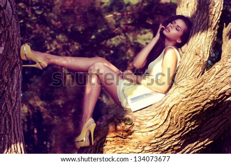 Young Sexy Woman In Yellow Dress Sitting On A Tree Branch. Summer Fashion Portrait