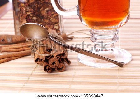 closeup of tea spoon lying on cinnamon sticks against glass of tea and bottle with tea leaves