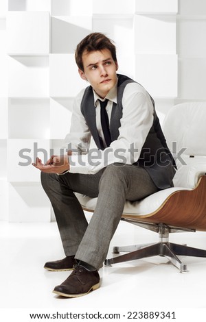 young stylish dressed man sitting in armchair in modern interior and thinking
