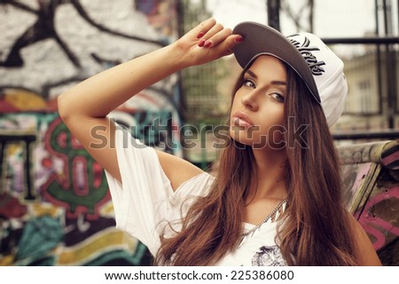 Portrait of young beautiful skater girl posing at city streets with graffiti. Fashion style portrait.