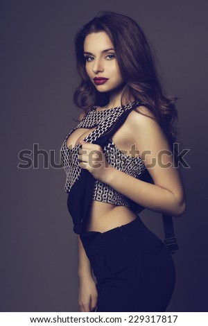 Fashion style portrait of young sexy female model posing against black background. Sensual girl with long dark curly hair and red lips