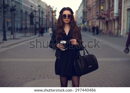 Young beautiful pretty girl walking along the street with handbag and cup of coffee.