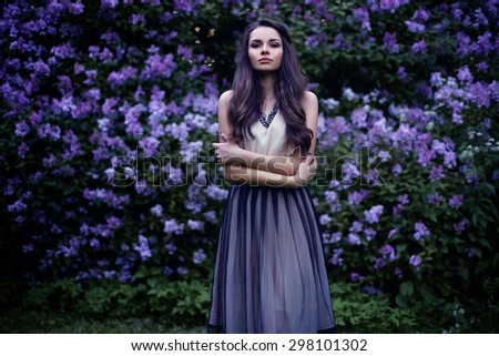 Fashion portrait of young beautiful pretty girl posing against lilac bushes in blossom