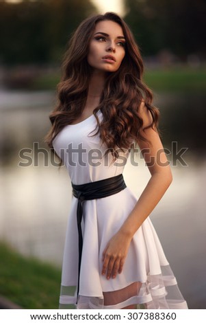 Outdoor portrait of young pretty beautiful calm woman posing outdoors in park in the evening. Elegant sexy girl wearing white summer dress.