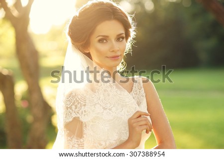 Wedding. Young beautiful bride with hairstyle and makeup posing in white dress and veil. Soft sunset light summer portrait. Girl looking in camera
