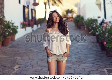 Young beautiful cheerful woman walking on old street at tropical town. Pretty girl looking at you and smiling