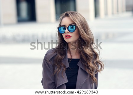 Outdoor closeup fashion style portrait of young pretty stylish girl with long curly hair wearing sunglasses