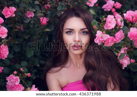Fashion style beauty romantic portrait of young pretty beautiful woman with long curly hair posing between pink roses. Stunning girl looking at you or in camera