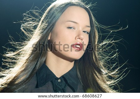 young beautiful woman with magnificent hair in motion and back light on black background