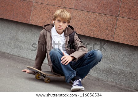 School teen sits on skateboard near school, day
