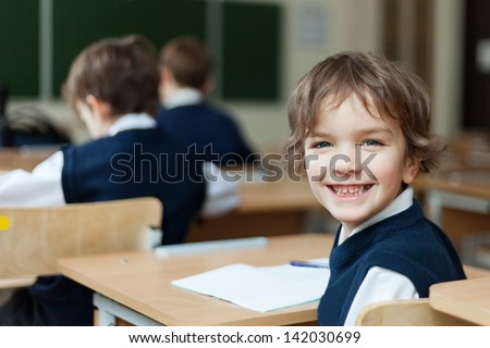 Happy Pupil in uniform sitting at  desk in school classroom