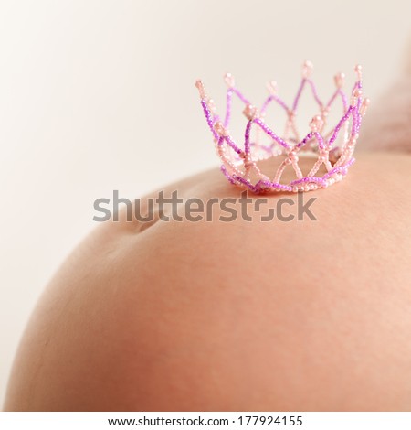 Belly of a young pregnant woman with  pink crown
