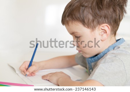 Serious pensive pupil sits at desk, writing in notebook, class, indoor