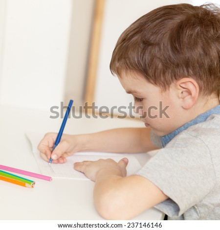 Serious pensive pupil sits at desk, writing in notebook, class, indoor